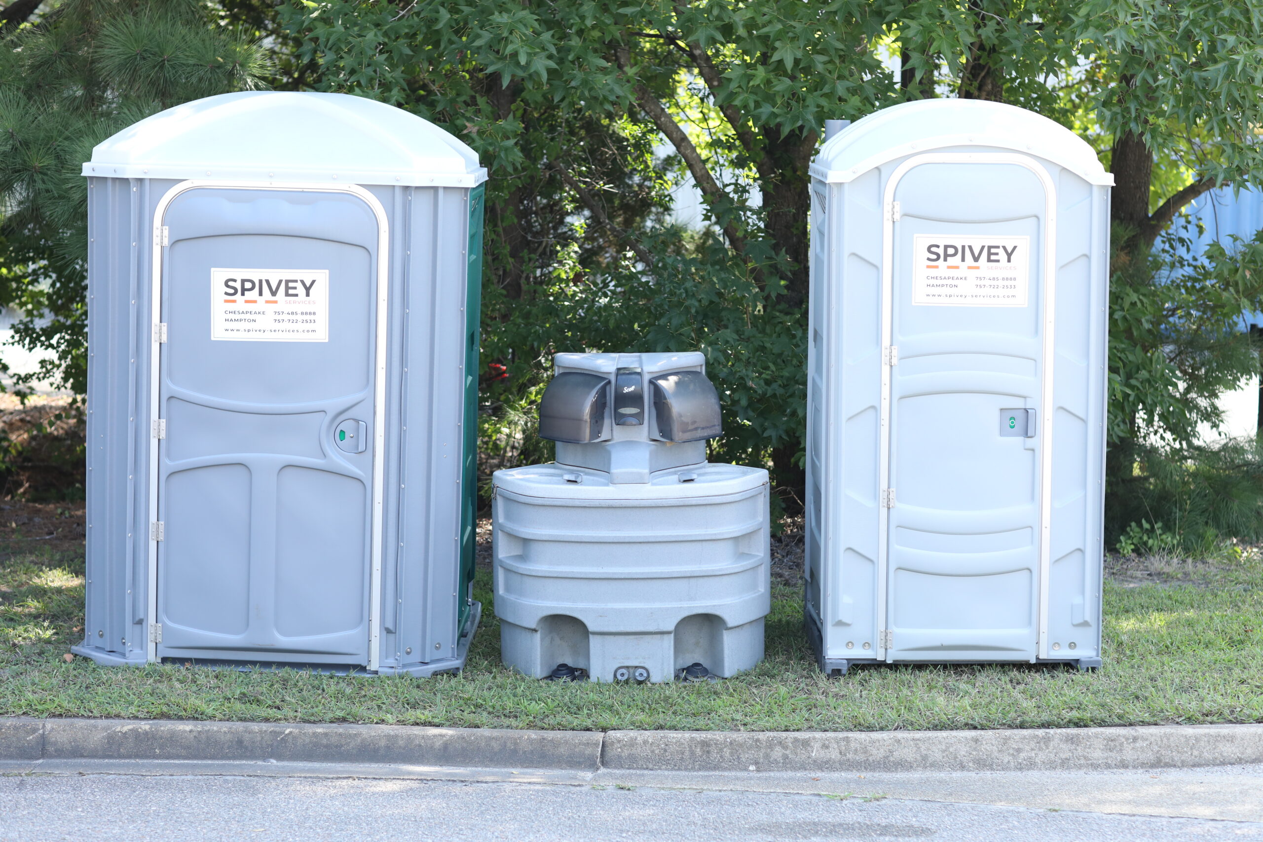 Spivey Services sanitation rentals for construction featuring two portable toilets and a central handwashing station.