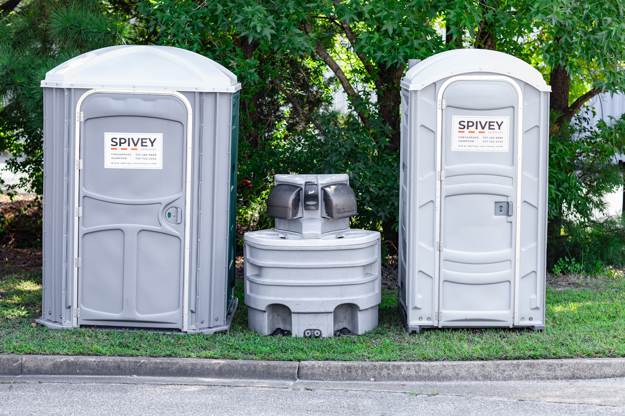 Portable toilets set up for outdoor festival with handwashing stations and crowd area nearby