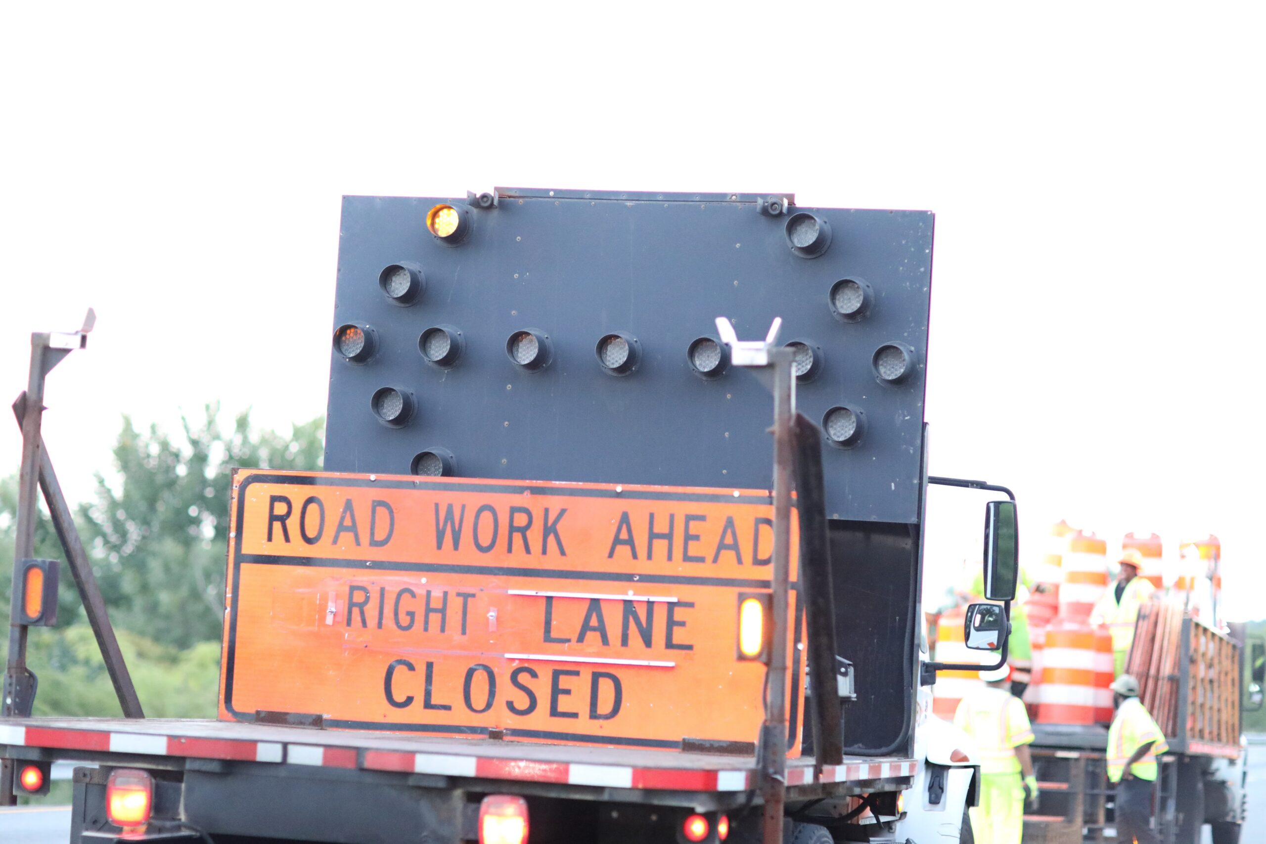 Traffic control sign indicating "Road Work Ahead" and "Right Lane Closed," with construction workers and equipment in the background, emphasizing traffic management for construction projects in Virginia.