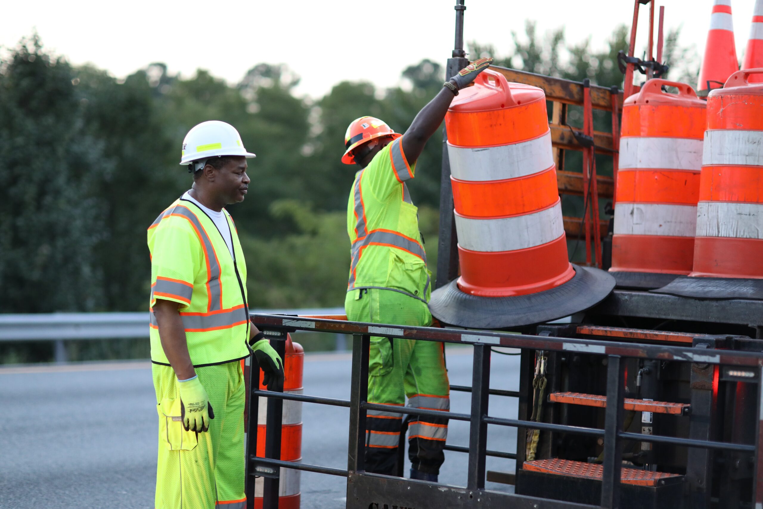 Construction workers in safety gear removing orange traffic cones from a truck bed, setting up an MUTCD safety work zone